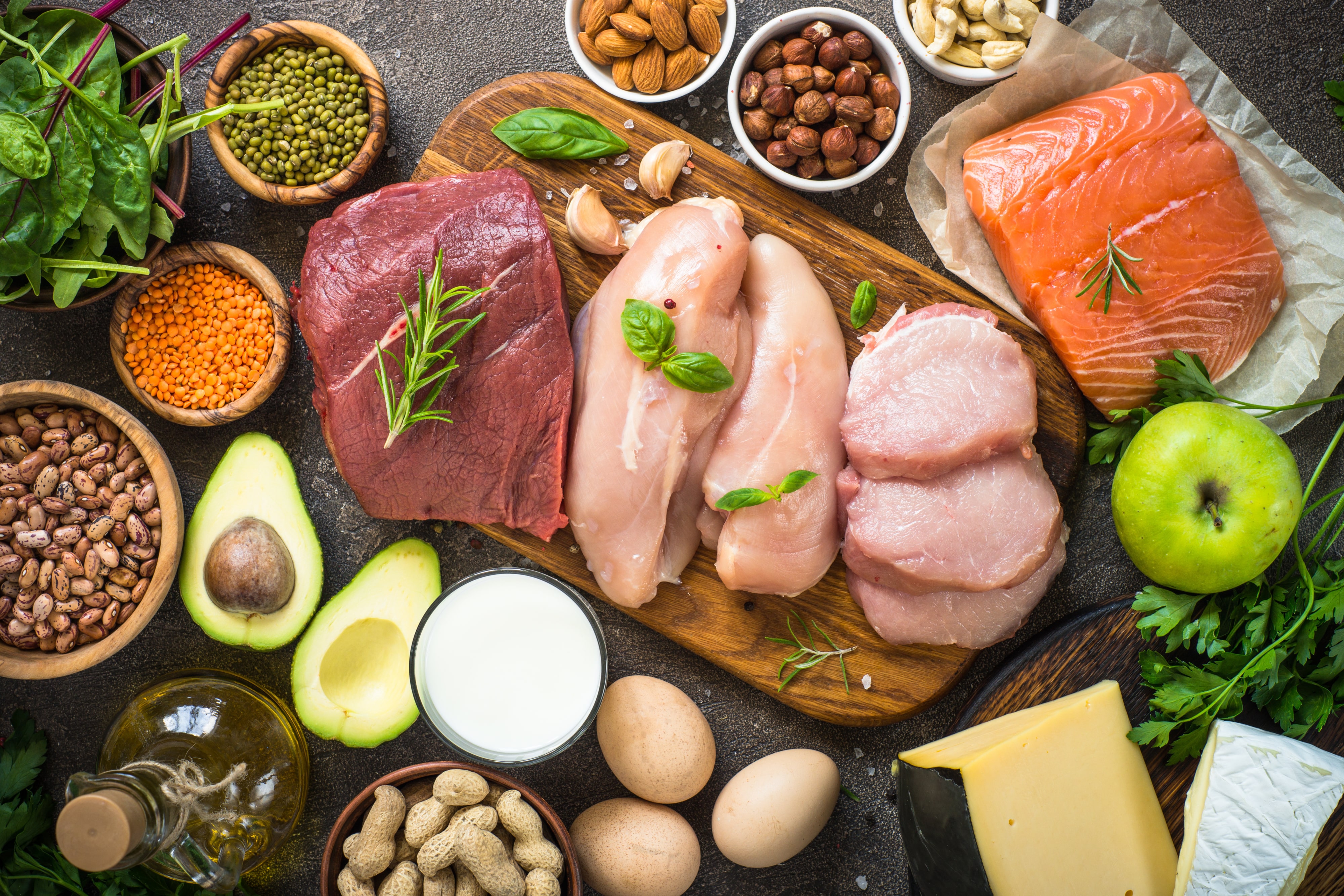 Protein sources. Meat, fish, eggs, cheese, milk, nuts, greens oil beans and lentils Top view on dark stone table