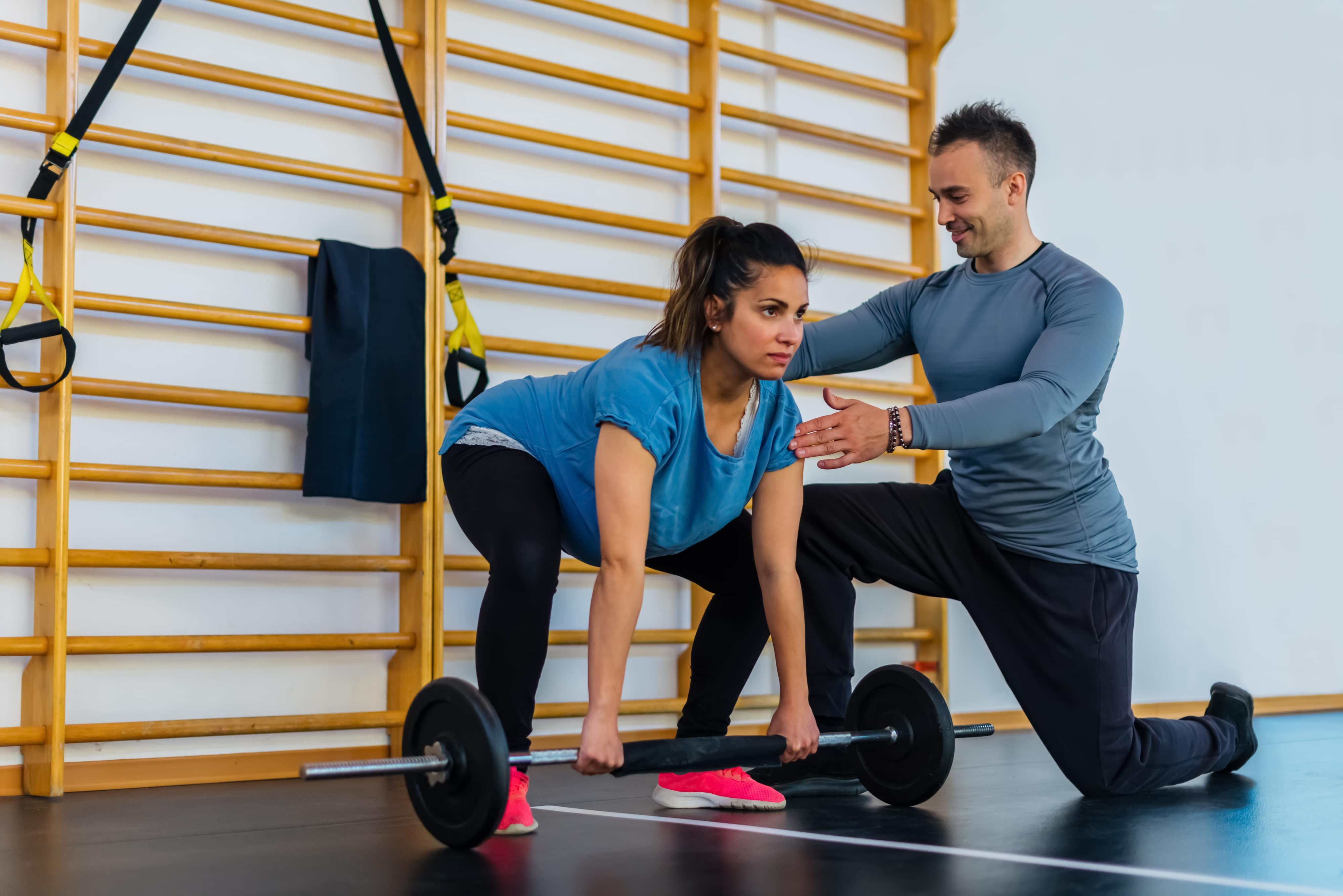 pregnant woman in blue shirt deadlifting a barbell with personal trainer next to her